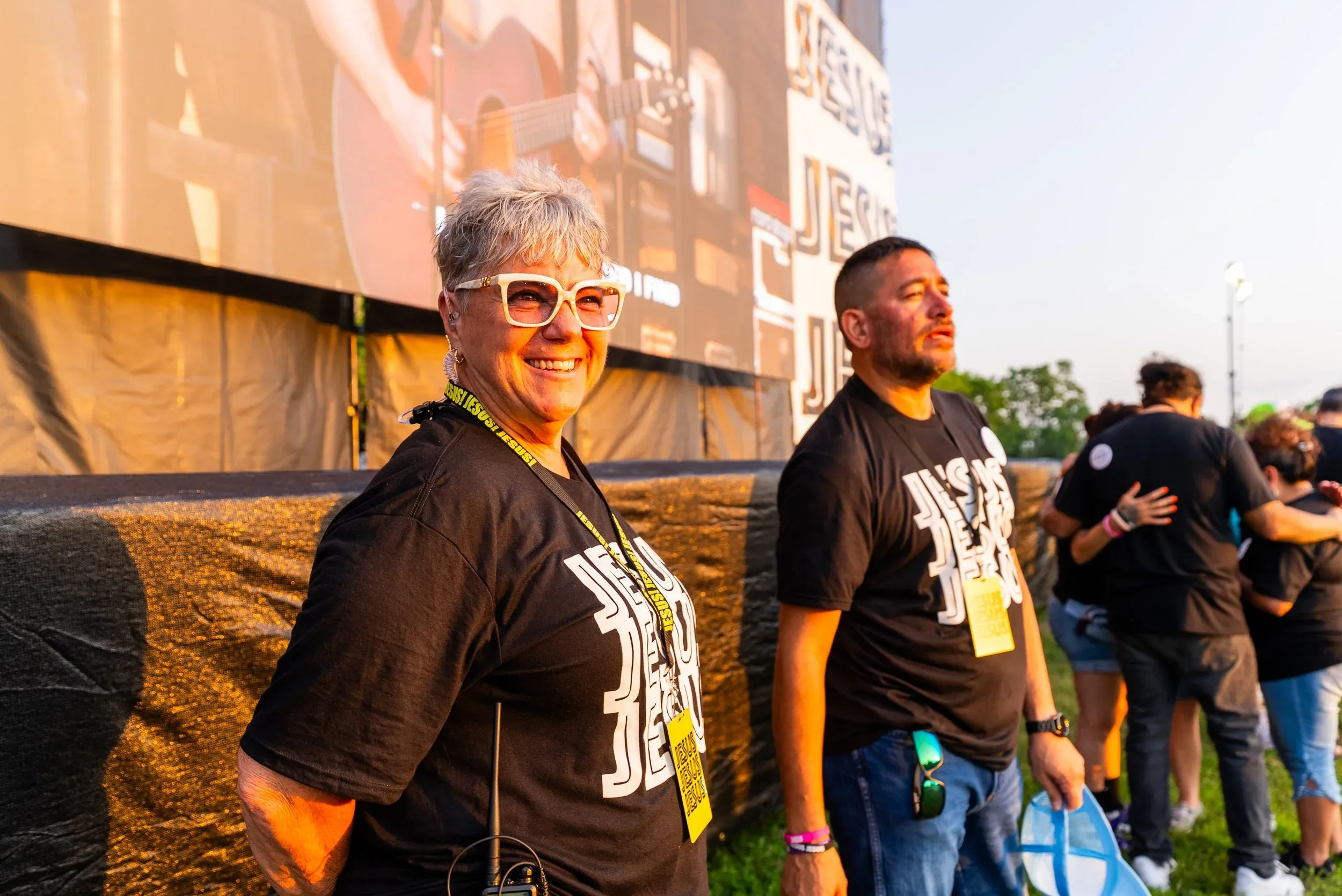 Two smiling volunteers in JESUS, JESUS, JESUS shirts