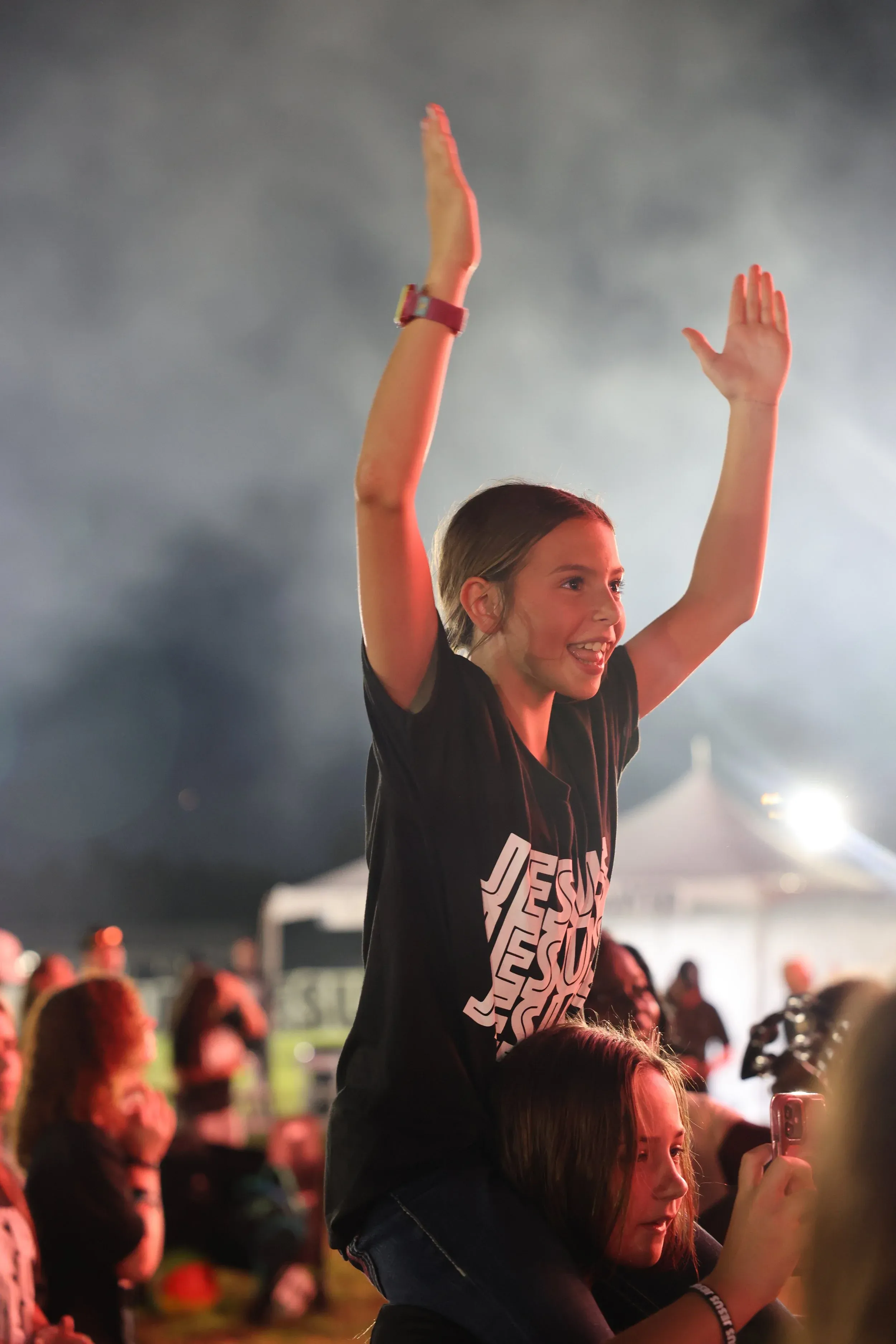 A child in a JESUS shirt with an arm raised at golden hour